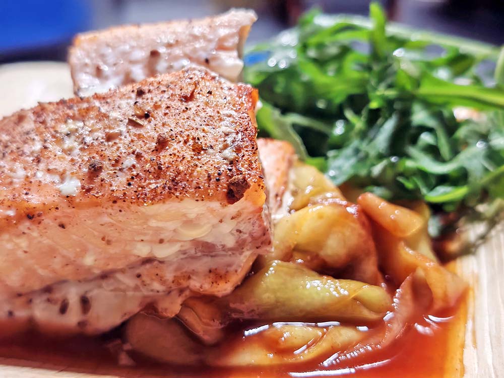 Nahaufnahme von zwei gebratenen Lachsfilets, serviert auf gebratenem Gemüse in Sauce, mit frischem Blattgemüse als Beilage.