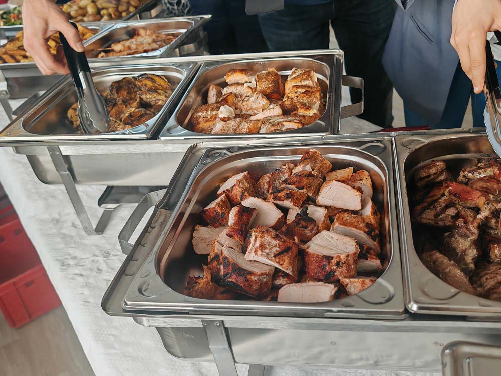 Mehrere Tabletts mit verschiedenen gegarten Fleischsorten sind in Buffetform angeordnet, und die Gäste bedienen sich mit einer Zange. Die Speisen werden in Chafing Dishes aus Edelstahl auf einem weißen Tischtuch präsentiert.