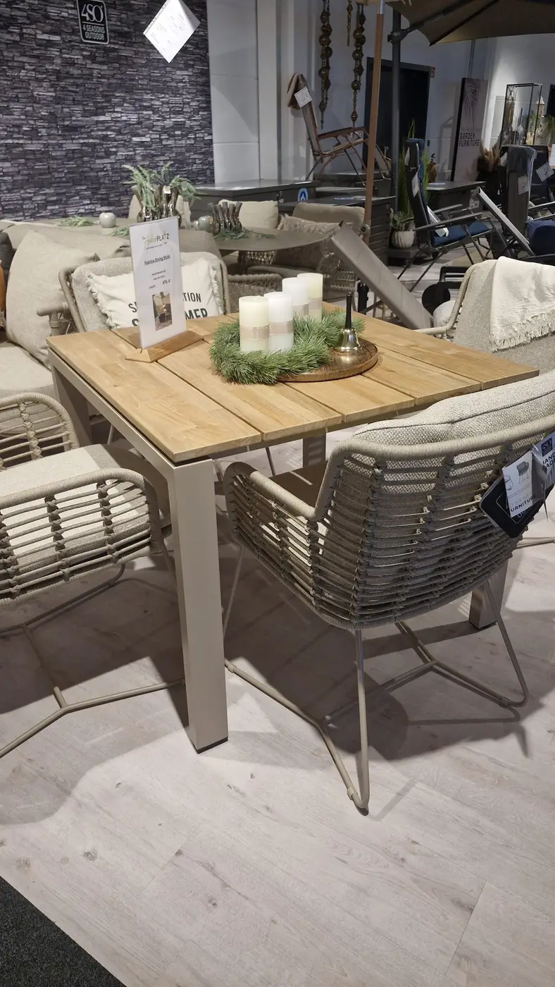 Goa Dining Tisch 160x95cm mit vier gepolsterten Stühlen, Kerzenständer und dekorativem Grün.