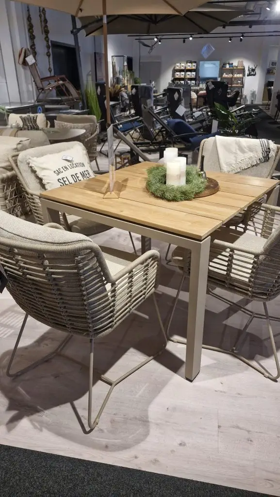 Der Goa Dining Tisch quadratisch wird mit vier geflochtenen Stühlen, Kerzen und Kissen in einem Möbelhaus ausgestellt.