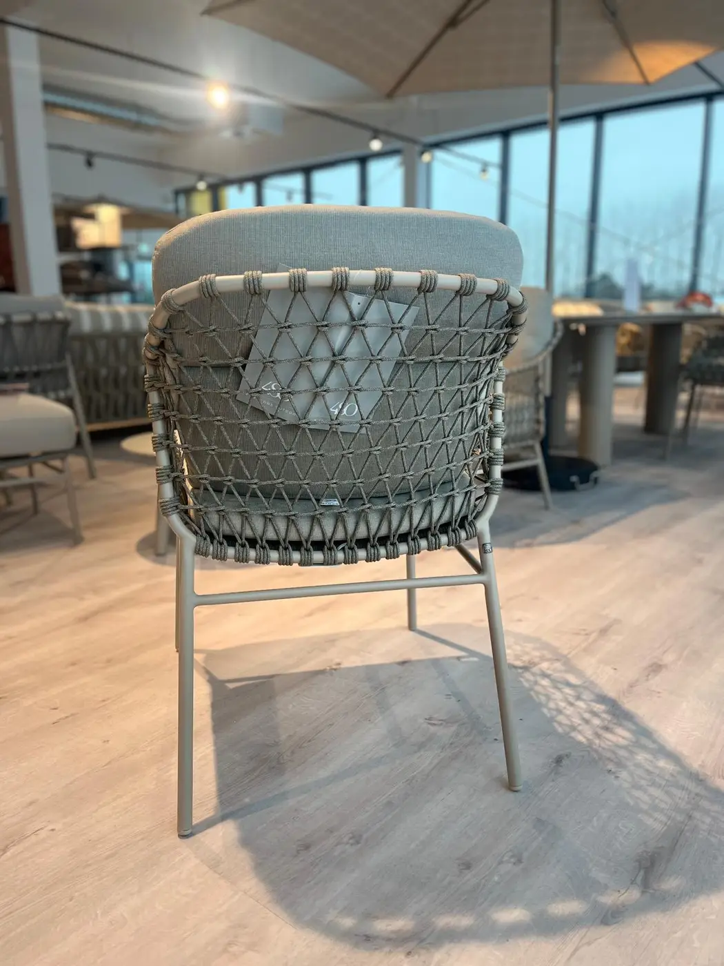 Der Kos Dining Stuhl mit Kissen steht auf einem Holzboden in einem modernen, sonnendurchfluteten Raum mit großen Fenstern.