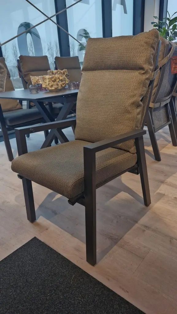 Palau Diningstuhl Khaki mit schwarzem Metallrahmen in einem modernen Raum in der Nähe eines Tisches und große Fenster.