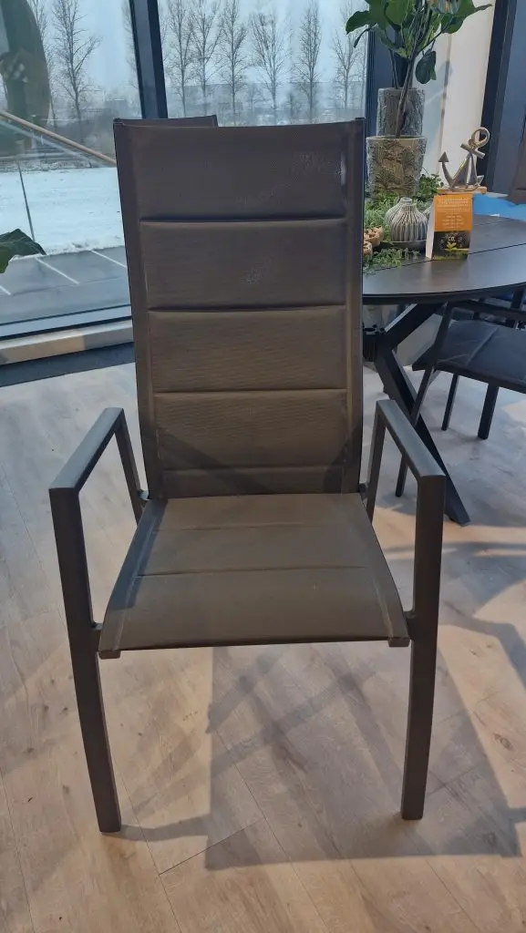 Der Palau Diningstuhl Khaki ist ein moderner Stuhl mit Armlehnen, der auf einem Holzboden an großen Fenstern steht.