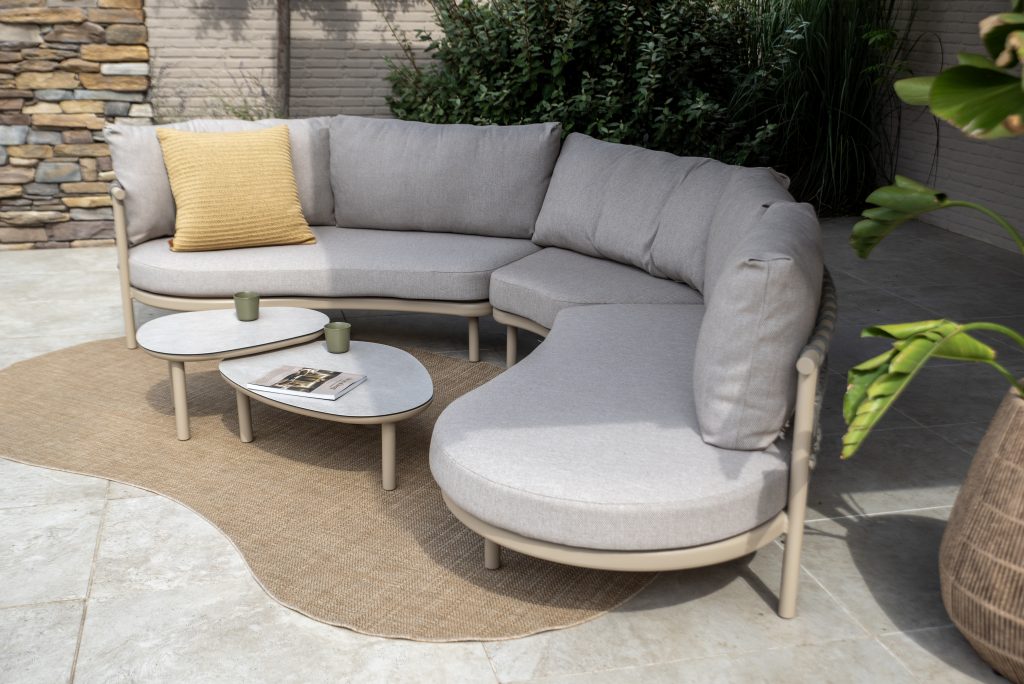 Gebogenes hellgraues Outdoor-Sofa mit gelbem Kissen und Monroe Kaffetisch-Set auf einer Terrasse.