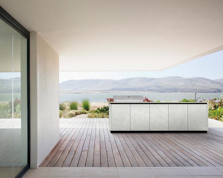 Moderne Außenküche auf einer Holzterrasse mit malerischem See- und Bergblick im Hintergrund.