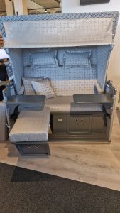 Strandkorb Konsul - Musterabverkauf: grau gepolsterter Strandkorb mit Sonnendach, Fußstützen, Kissen & faltbarem Tablett. Gartenmöbel und Grills kaufen in Rostock, Mecklenburg-Vorpommern.