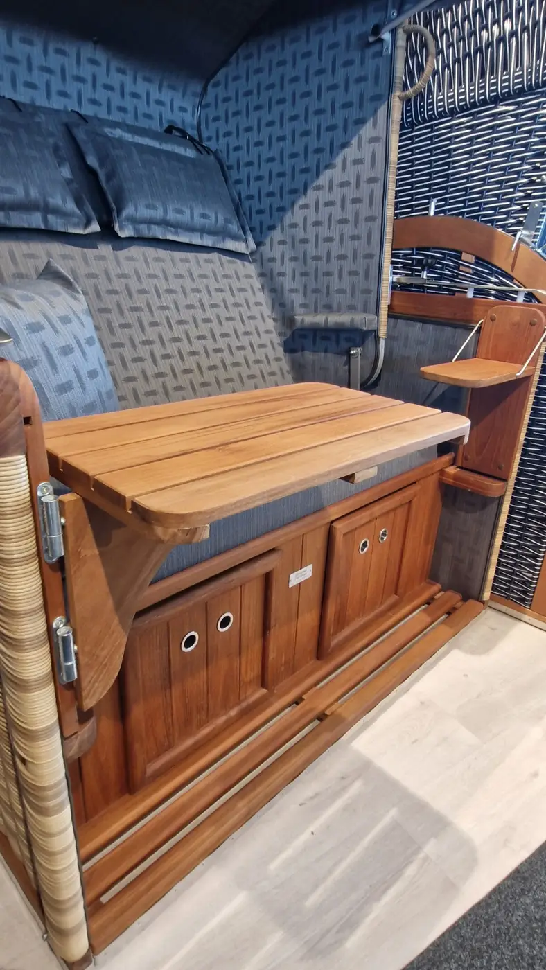 Holztisch und klappbarer Sitz mit Kissen in einem Strandkorb Präsident Teak - Musterabverkauf auf hellem Holzboden. Gartenmöbel und Grills kaufen in Rostock, Mecklenburg-Vorpommern.