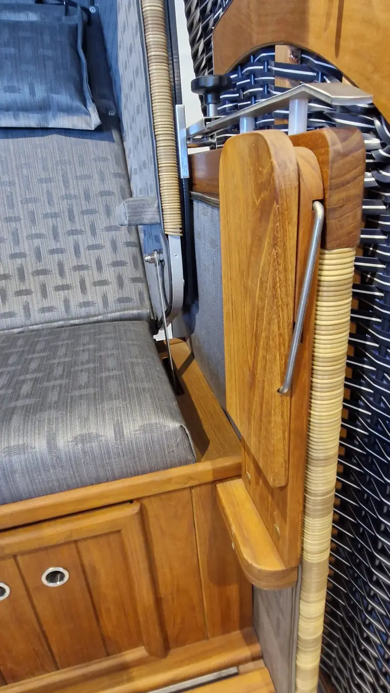 Nahaufnahme von Strandkorb Präsident Teak - Musterabverkauf Armlehne mit klappbarem Tablett neben gemustertem gepolstertem Sitz. Gartenmöbel und Grills kaufen in Rostock, Mecklenburg-Vorpommern.